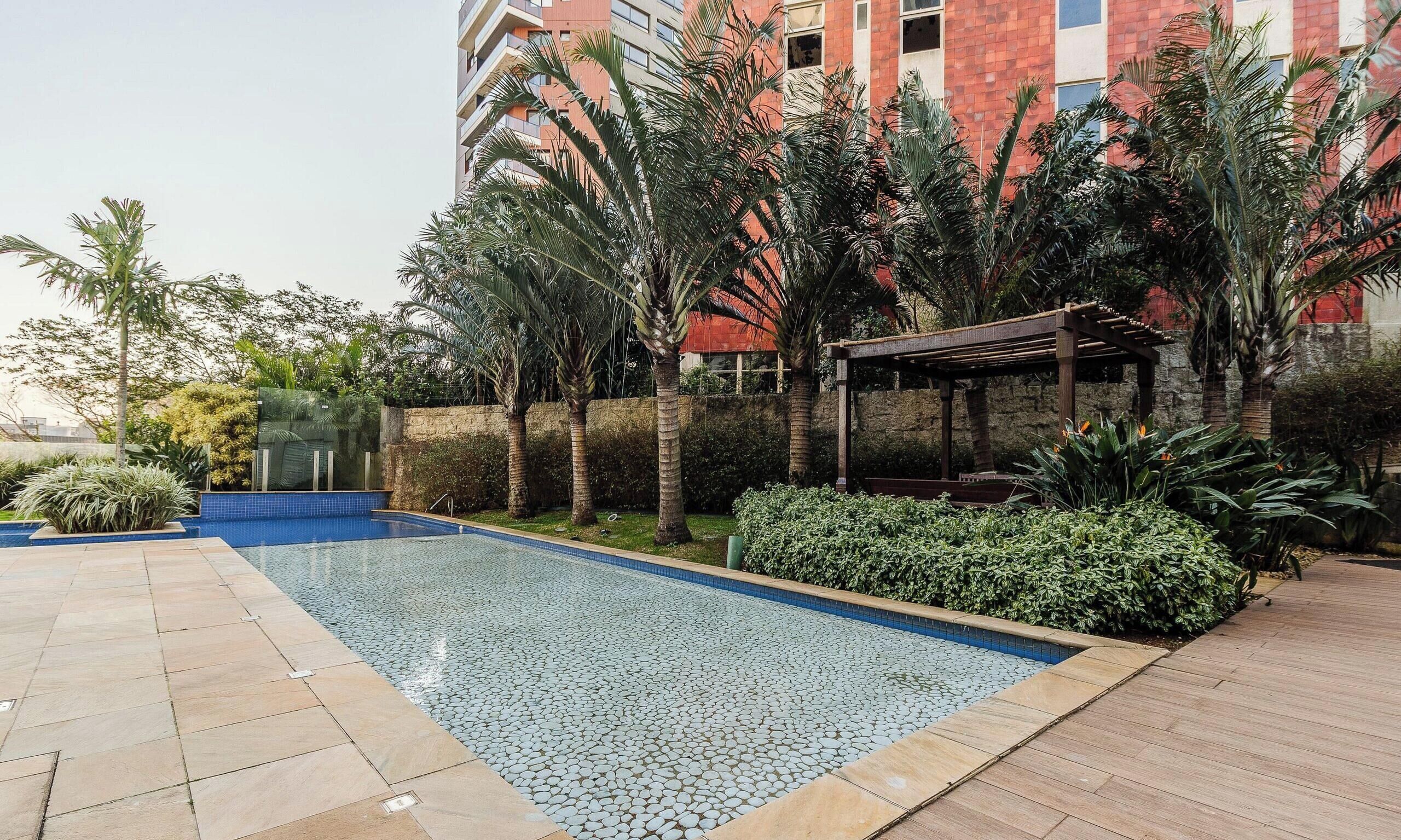 A swimming pool with a pebble pattern, surrounded by palm trees and a wooden pergola.