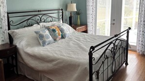 Une chambre à coucher comprenant un lit, une table de chevet, une lampe, un ventilateur de plafond et une fenêtre avec des rideaux.
