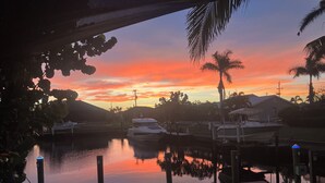 Un port de plaisance au coucher du soleil, avec des bateaux amarrés, un espace de détente au bord du quai et des palmiers.