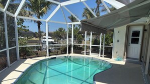 Une piscine à l’eau d’un bleu cristallin, entourée d’une structure de verre offrant une vue sur des palmiers et un bâtiment blanc en arrière-plan.