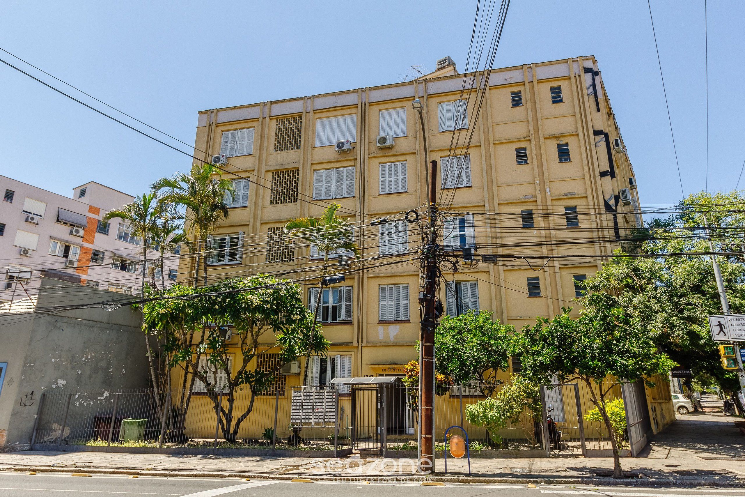 A multi-story building with a yellow facade, air conditioning units, and a gated entrance.