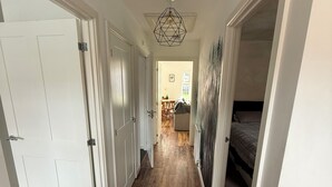 Un couloir doté d’un plancher en bois, de murs blancs et d’un luminaire au plafond.