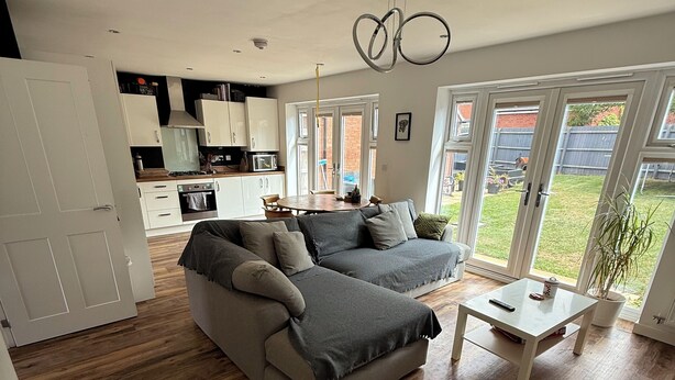 Un salon moderne avec un canapé d’angle gris, une petite table blanche et une cuisine en arrière-plan.