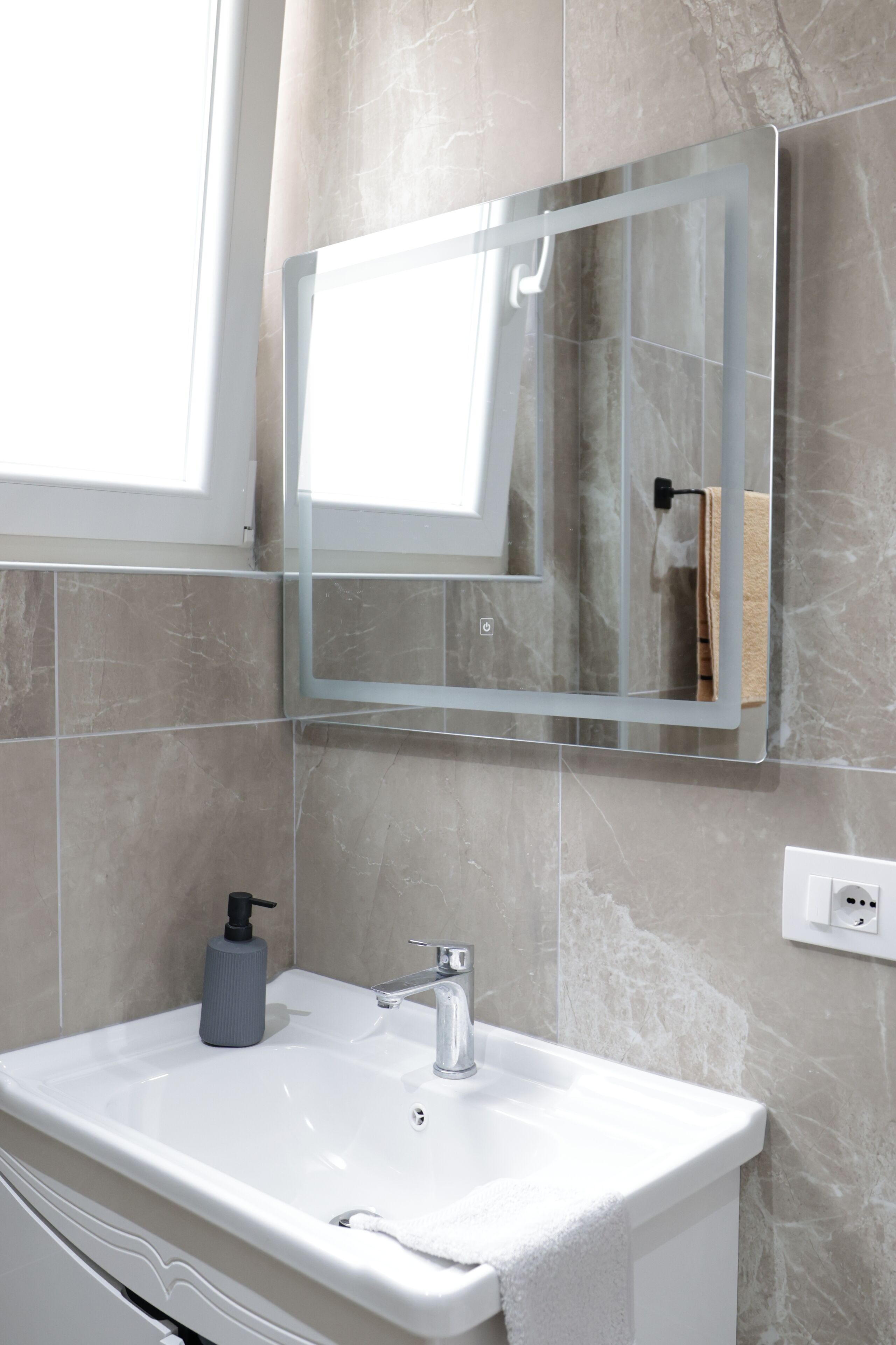 Un baño con lavamanos blanco, espejo y perchero.