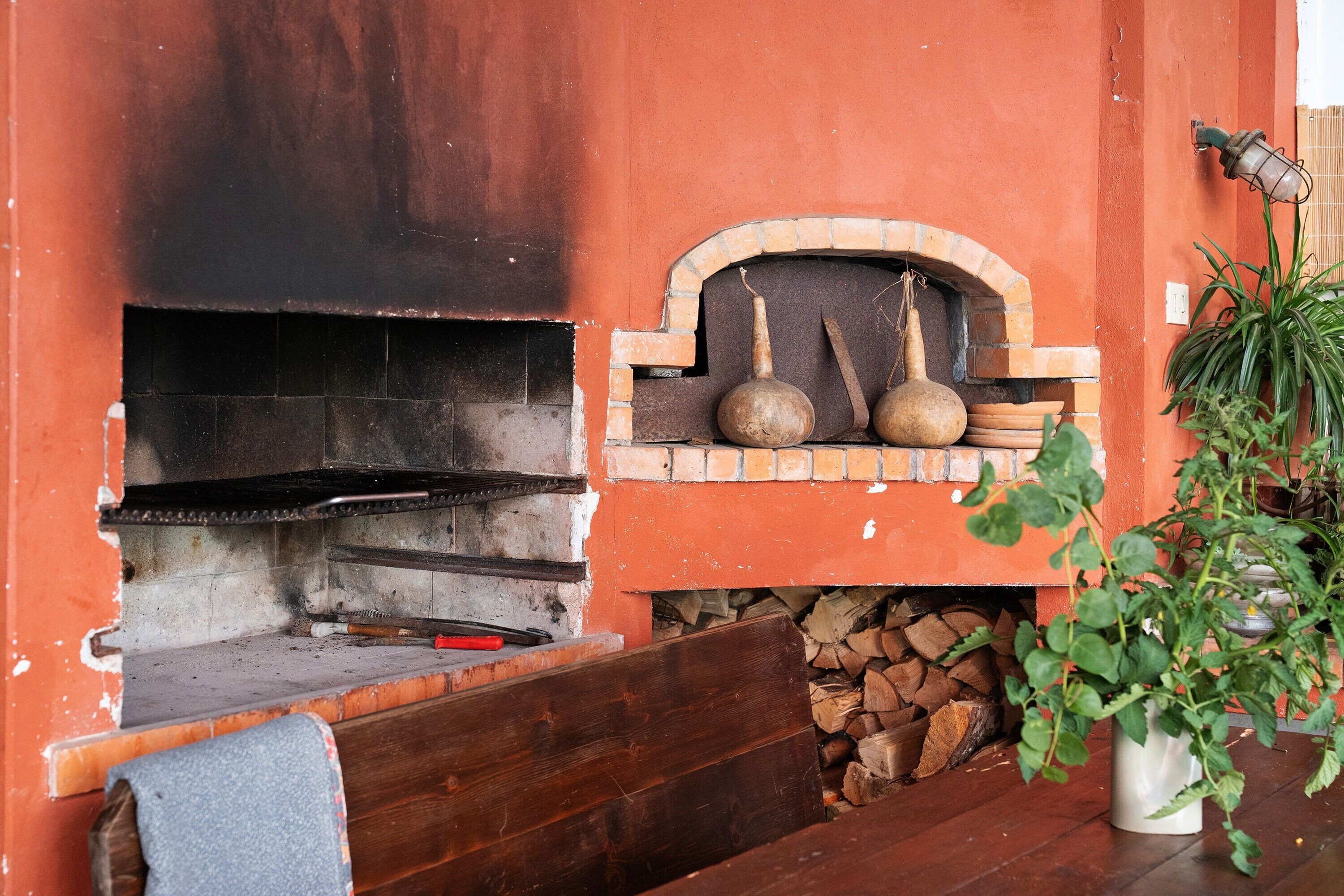 A brick oven with a wooden bench, a potted plant, and a hanging light fixture.