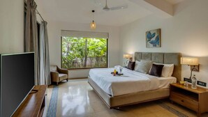 A modern hotel room with a large bed, a TV, a desk, and a window with a view of greenery.