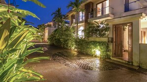 A modern building with a paved courtyard, surrounded by lush greenery and palm trees.