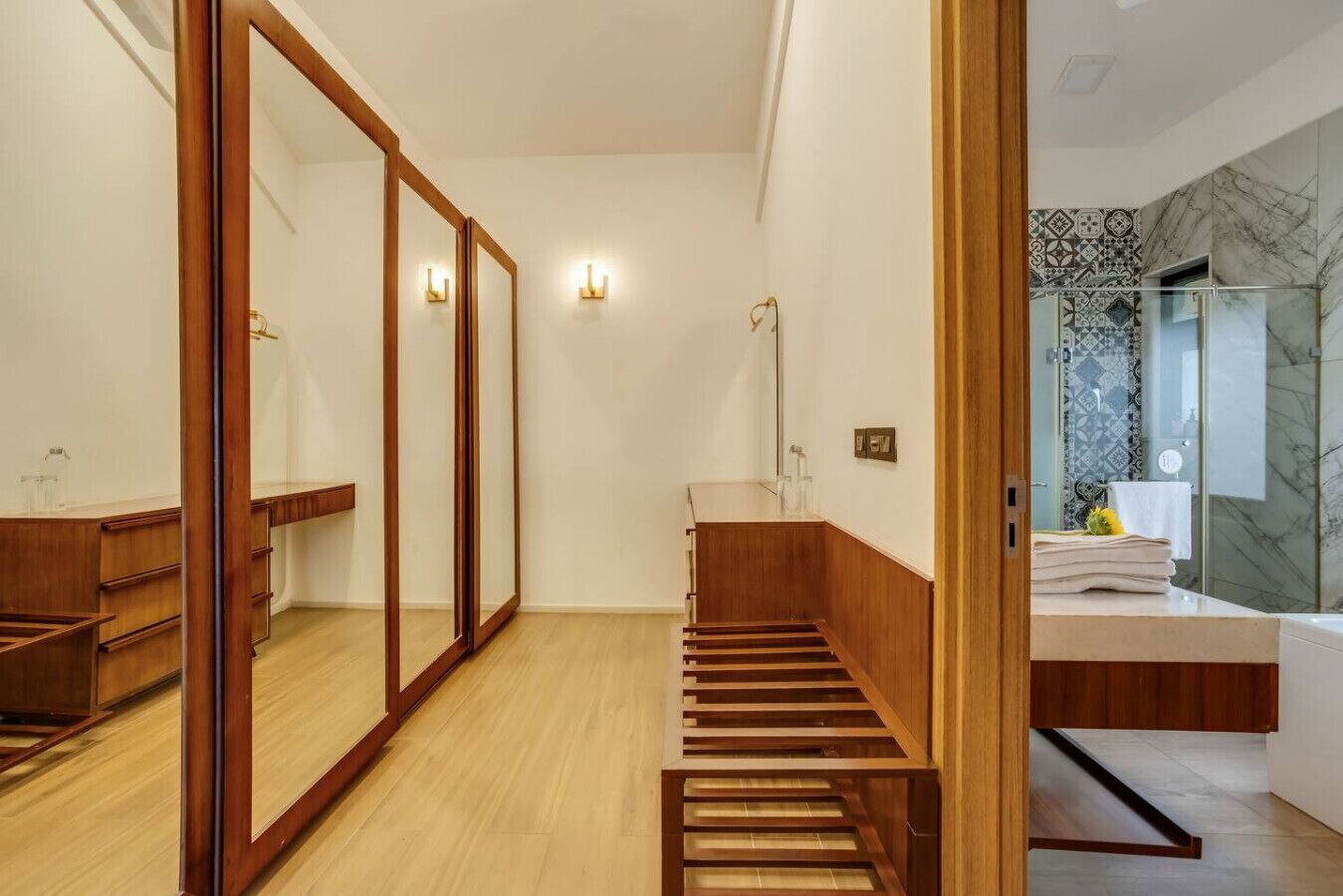 Een moderne badkamer met een houten wastafelmeubel, een grote spiegel en een douchegedeelte betegeld met marmer.