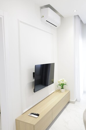 Una sala de estar moderna con un televisor montado, un mueble bajo de madera, un control remoto y una planta en maceta.