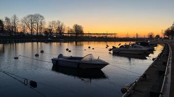 Een rustige rivier met aan de oever afgemeerde boten, een brug op de achtergrond en bomen langs de oevers.