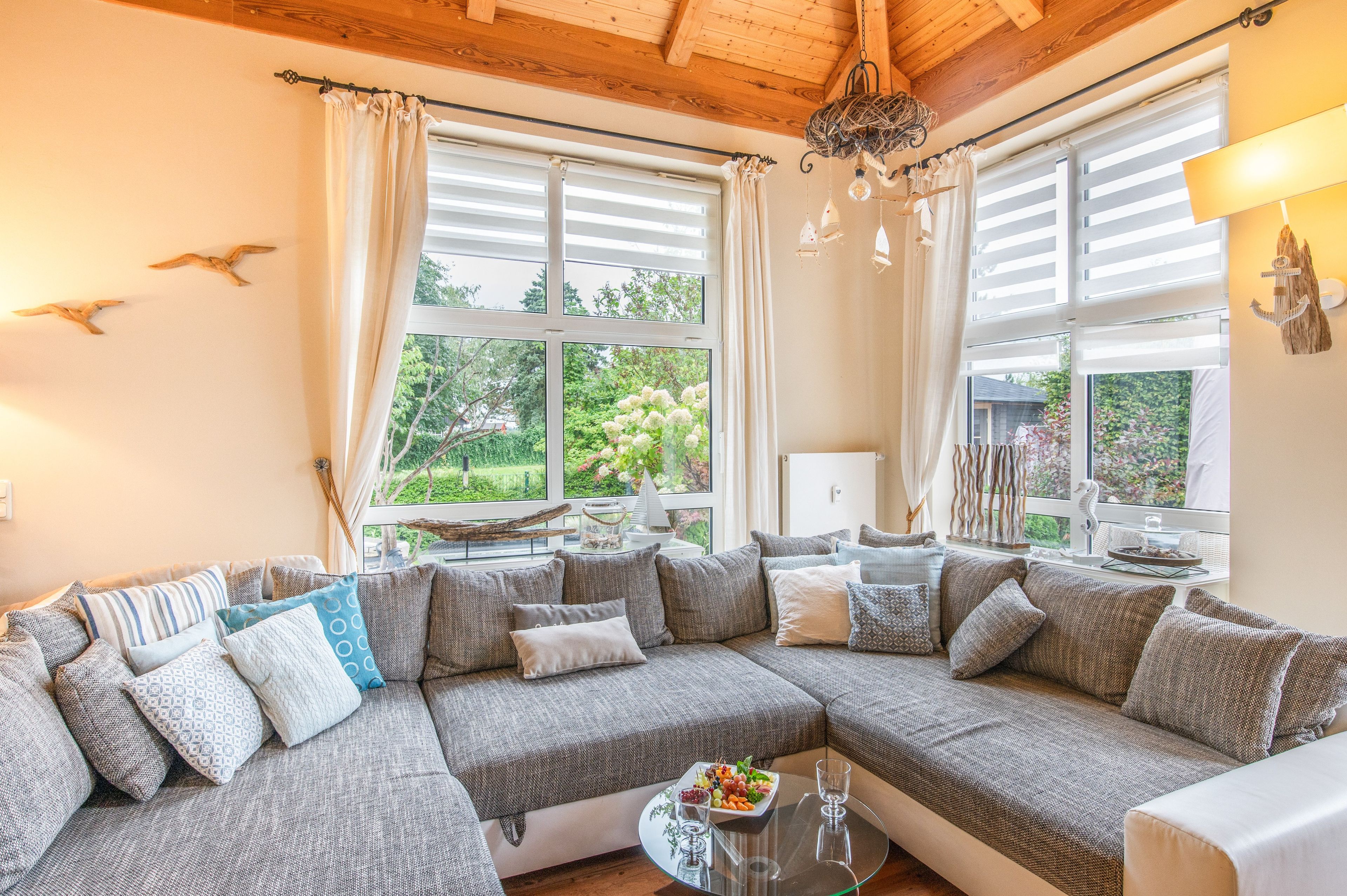 Ein gemütliches Wohnzimmer mit einem großen Ecksofa, einem Glastisch und Blick auf Grünflächen.