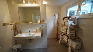 Un bagno con lavandino, specchio, portasciùmani e mensole con asciugamani.