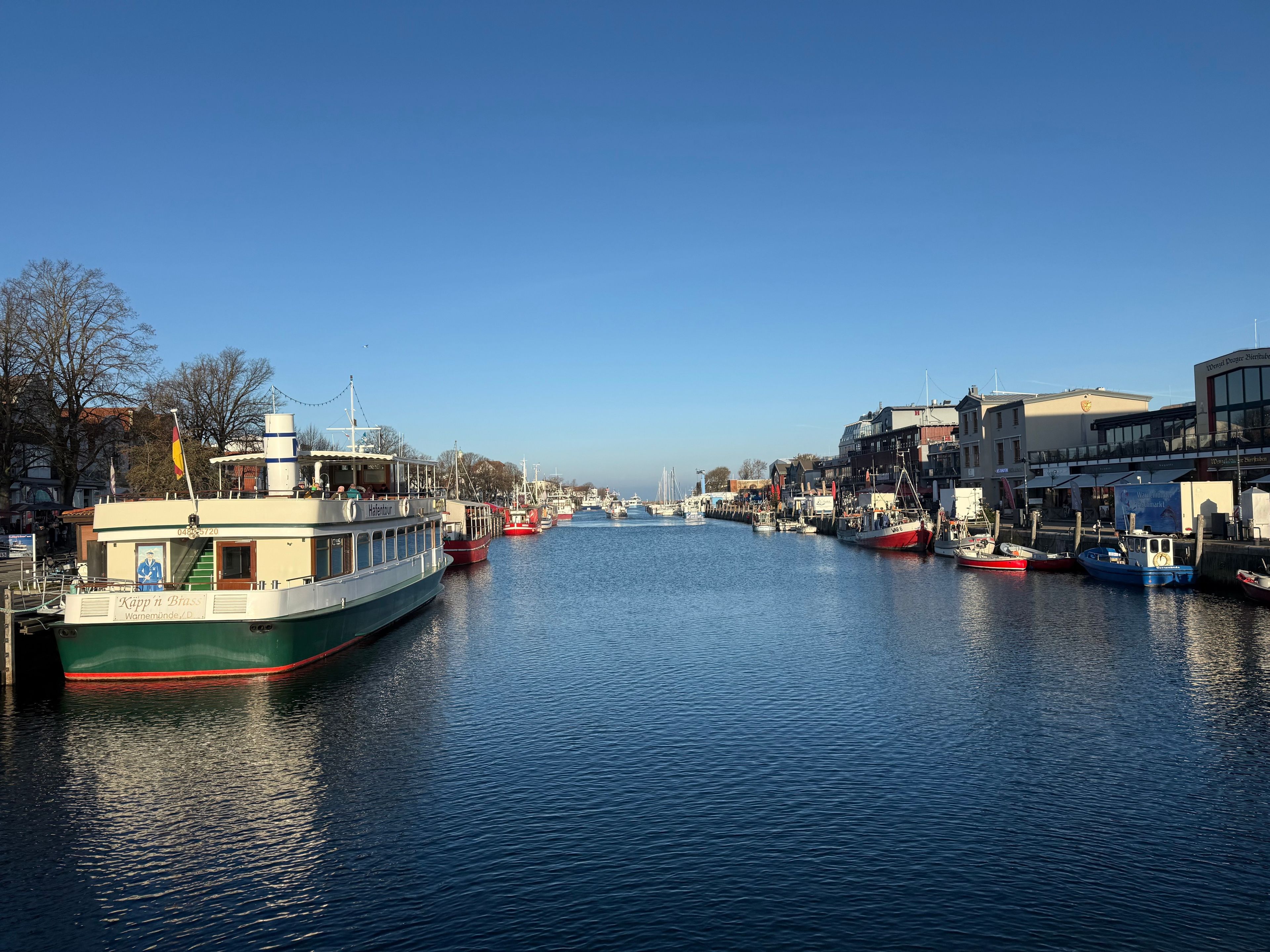A calm river with boats docked along the banks, surrounded by buildings and trees.