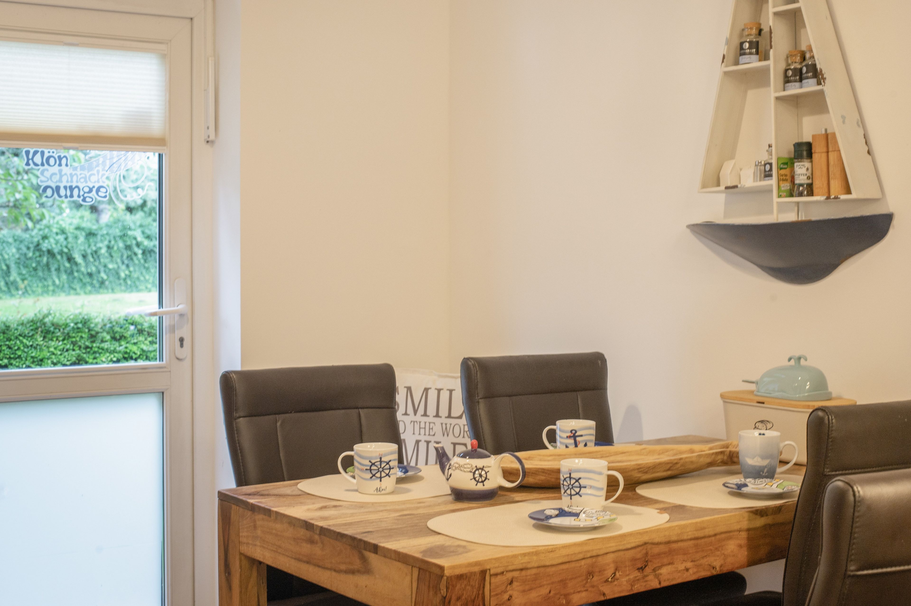 Ruokailutila, jossa on puinen pöytä kahdelle, kaksi tuolia ja hylly, jossa on erilaisia esineitä.
