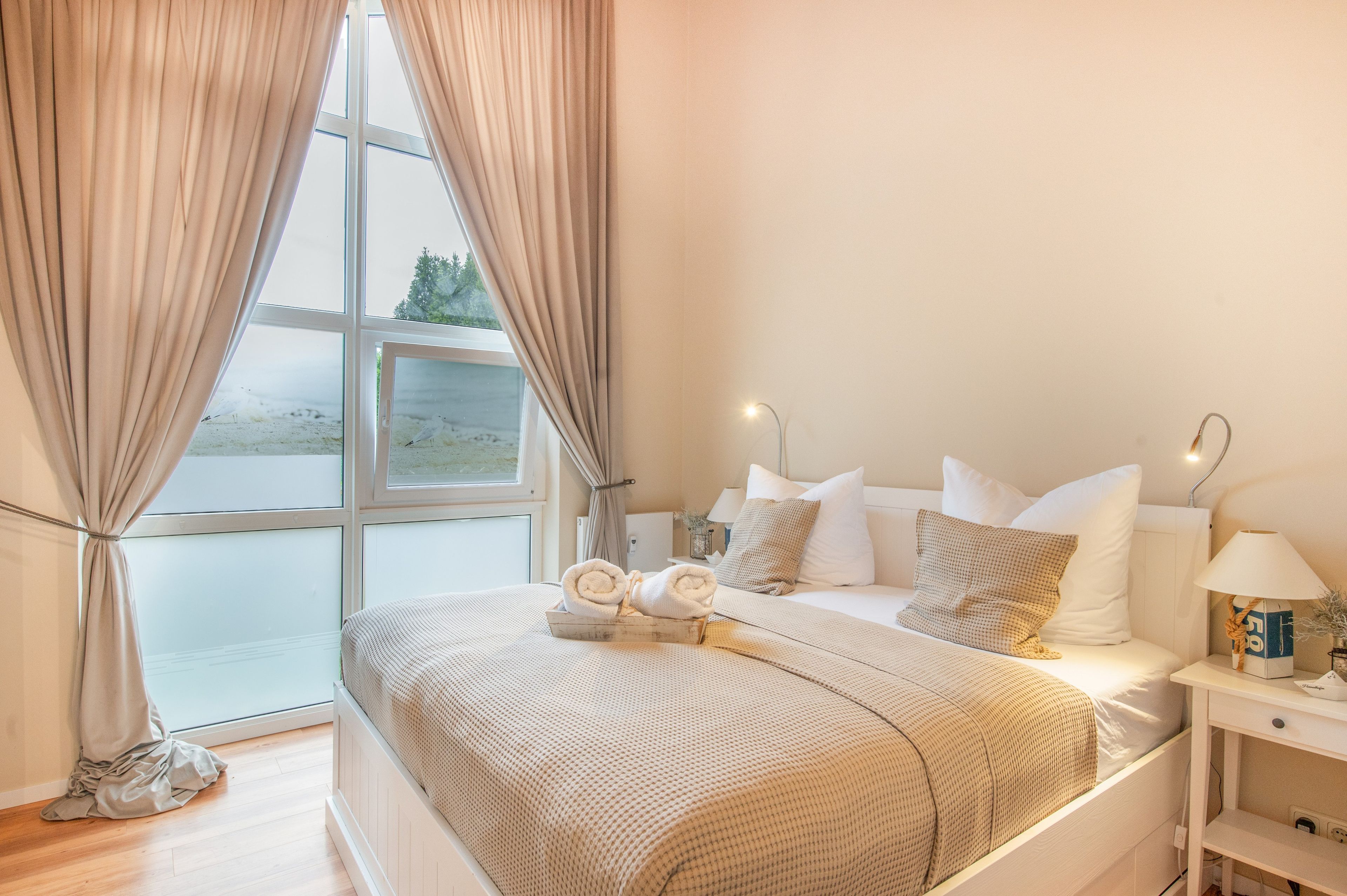 A bedroom with a bed, pillows, a nightstand, a lamp, and a window with curtains.