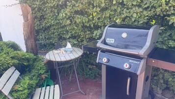 Un barbecue Weber doté de commandes, une petite table sur laquelle est posé un modèle de voilier, et un banc.