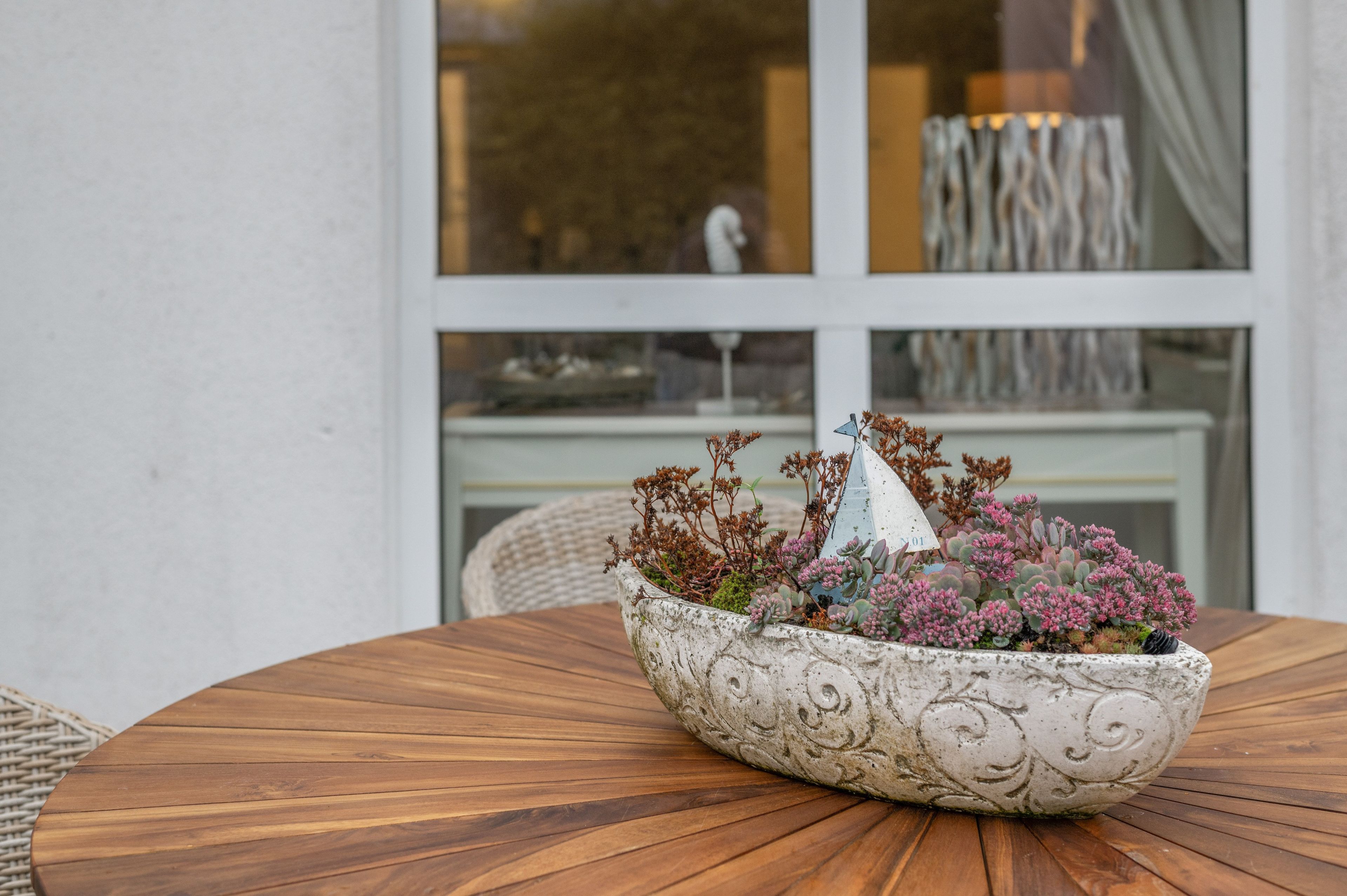 A round wooden table with a decorative bowl containing succulents and a small blue flag.