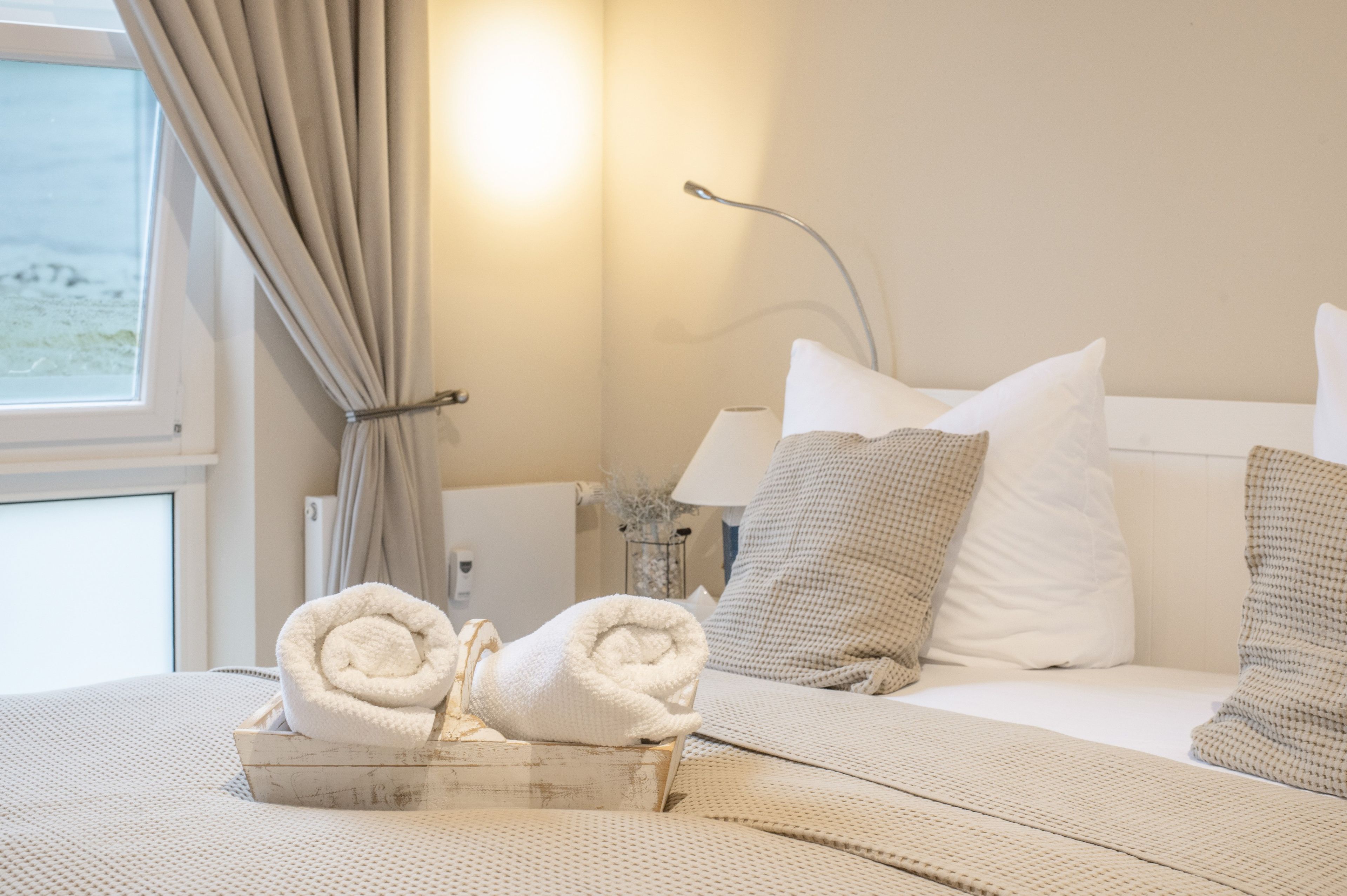 Een hotelkamer met een bed, kussens, een nachtkastje, een lamp en een raam met gordijnen.