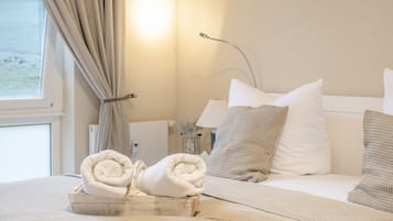 Een hotelkamer met een bed, kussens, een nachtkastje, een lamp en een raam met gordijnen.