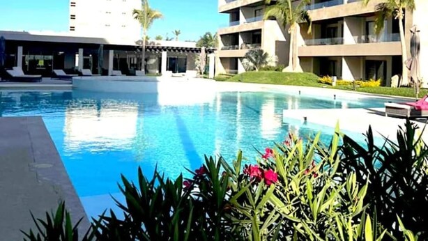 A hotel with a swimming pool, multiple balconies, and a clear blue sky. - Vista Vela Condo · Pool, Gym & Pickleball Courts (El tezal)