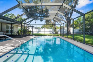 Piscina com estrutura de vidro, rodeada por gramado e árvores.