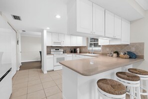Uma cozinha moderna com armários brancos, uma ilha central com banquetas e um micro-ondas acima da pia.
