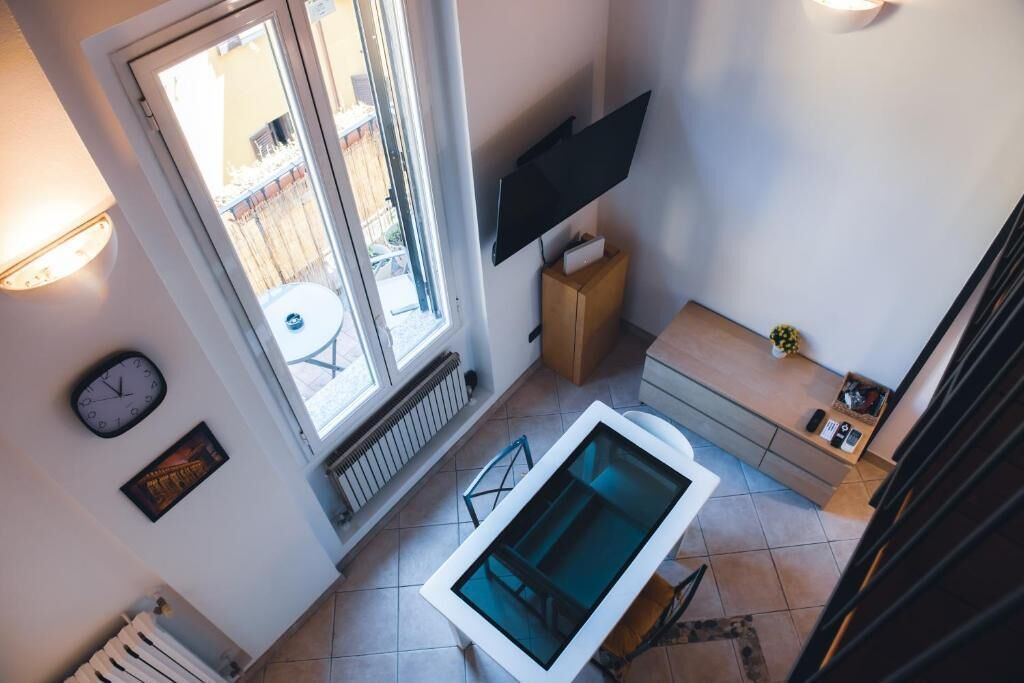 A compact living space with a large window, a flat-screen TV mounted on the wall, a small table, and a built-in bathtub.