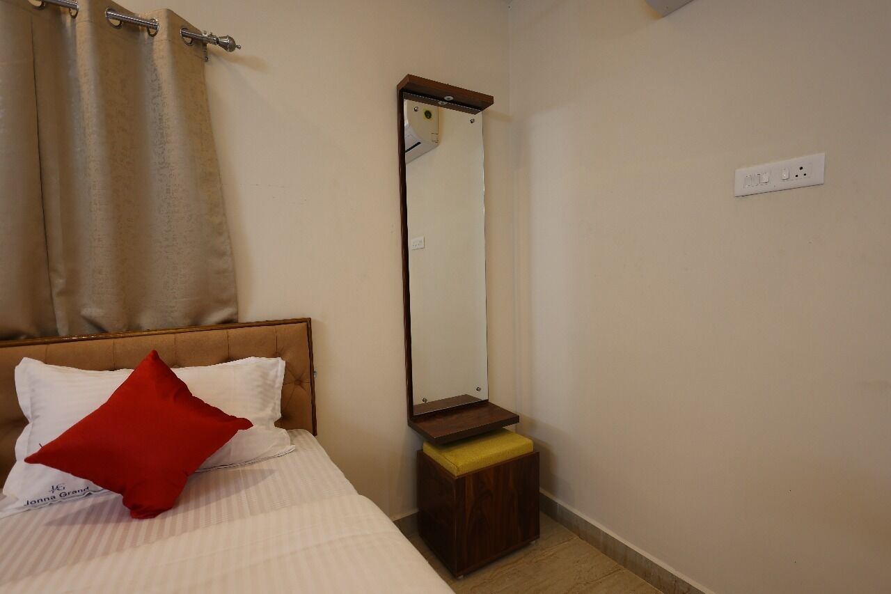 Une chambre à coucher avec un lit, un oreiller rouge, une table de chevet en bois avec un miroir et un rideau beige.