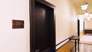 Un pasillo con una puerta de madera oscura, una placa de madera con un número y un banco.