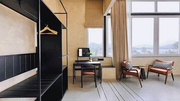 A room with a black sofa, a desk with a lamp, two chairs, a window with a view, and a hanging coat rack.