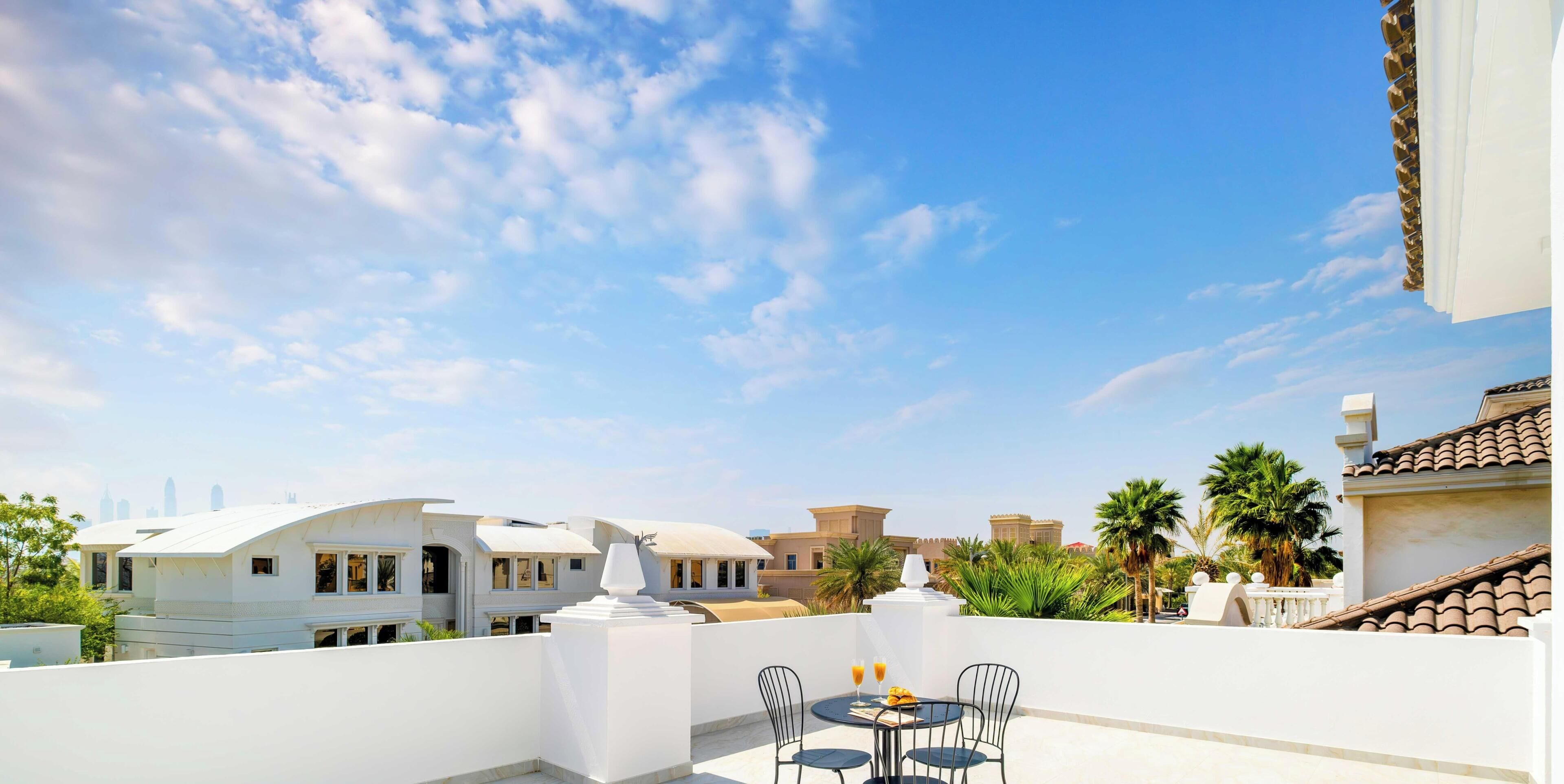 Une terrasse sur le toit, avec une table et des chaises, offrant une vue sur les gratte-ciel de la ville et agrémentée de palmiers.