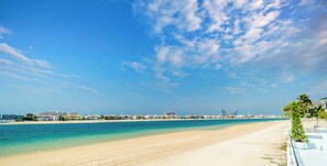 Een strand met heldere lucht, een zandstrand en een uitzicht op een stadsbeeld in de verte.