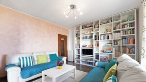 Un salon avec un canapé blanc, un canapé bleu, une table basse blanche et une bibliothèque remplie de livres et d’objets décoratifs.