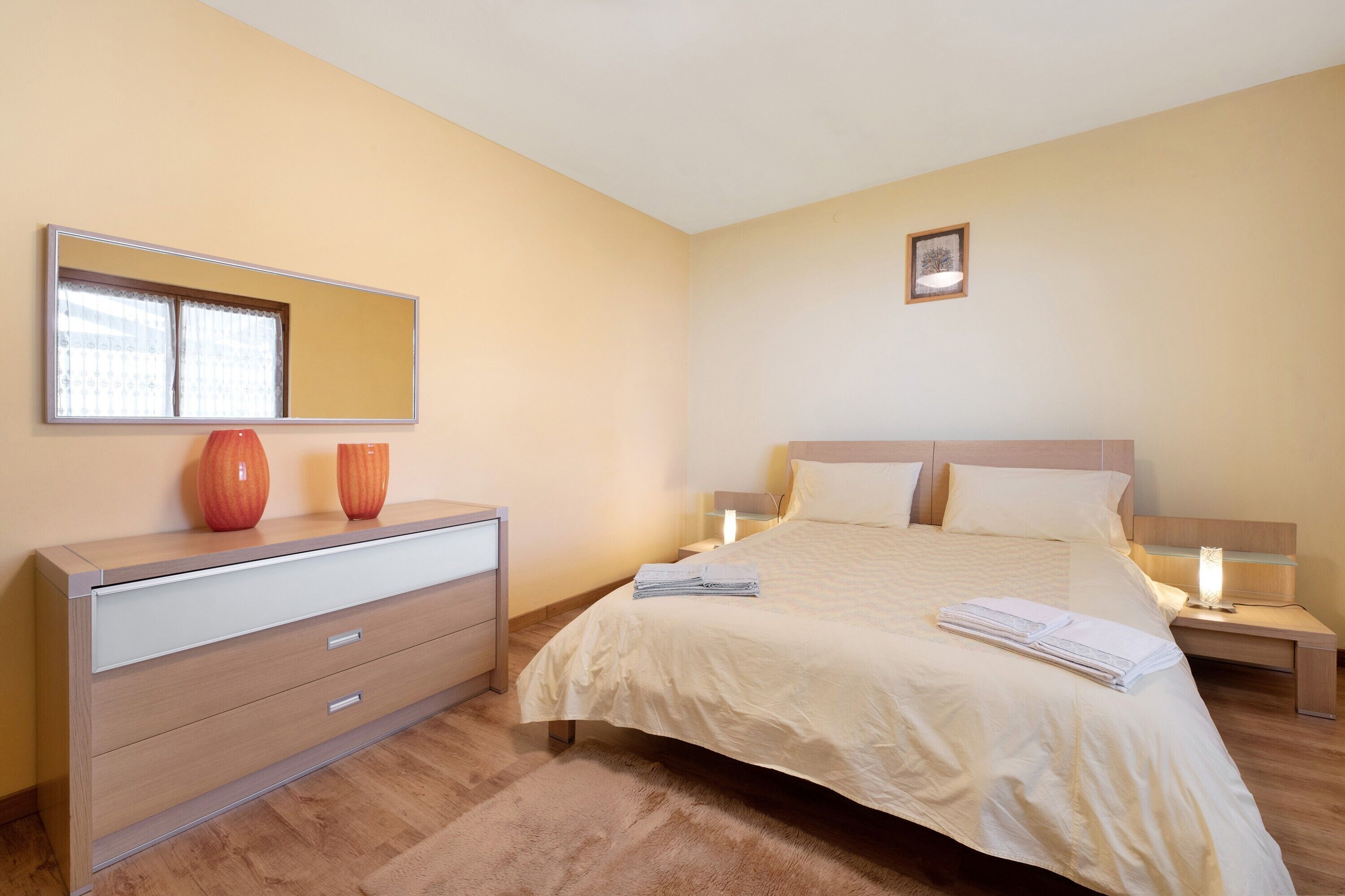 A bedroom with a bed, bedside tables, a dresser, a mirror, and a picture on the wall.