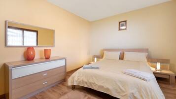 A bedroom with a bed, bedside tables, a dresser, a mirror, and a picture on the wall.