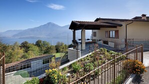 Une maison avec une terrasse, une vue sur les montagnes et un plan d’eau.