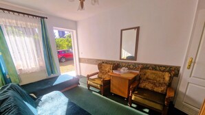 A room with a bed, two chairs, a small table with a cup and saucer, and a mirror on the wall.