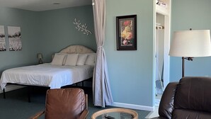 Un dormitorio con cama, una silla, una mesita y una lámpara.