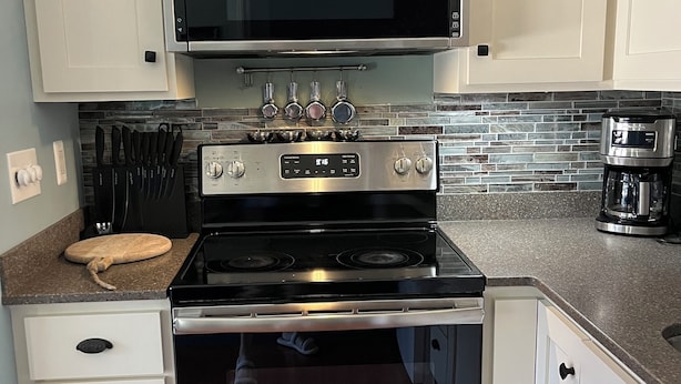 Una cocina con armarios blancos, estufa de acero inoxidable y microondas.