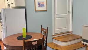 Un comedor con una mesa redonda de madera, dos sillas, un cuadro pequeño en la pared y una puerta blanca con un escalón que lleva a un rellano.