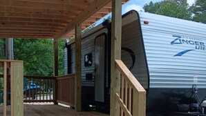 Une terrasse en bois mène à un porche abrité, à côté duquel est garavané un camping-car.
