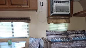 Un intérieur de camping-car compact comprenant un lit, une petite table et une fenêtre avec des stores.