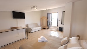 Ein modernes Hotelzimmer mit einem Bett, einer Couch, einem an der Wand befestigten Fernseher, einem Holzschrank und einem kleinen Tisch mit einer Schale.