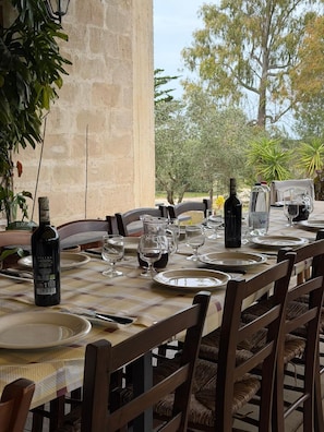 A table set for dining outdoors with a bottle of wine, glasses, and plates. - Agriturismo Pietragrande (Otranto)