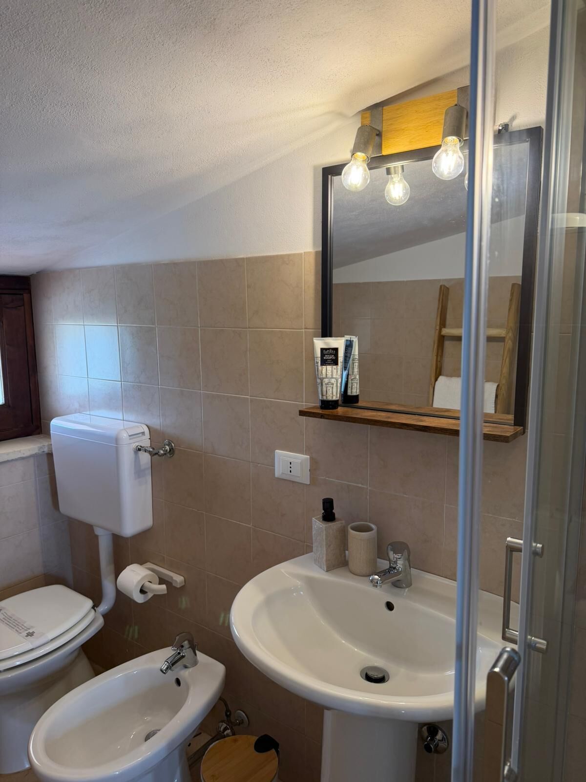 Ein Badezimmer mit Toilette, Bidet, Waschbecken und einem beleuchteten Spiegel.