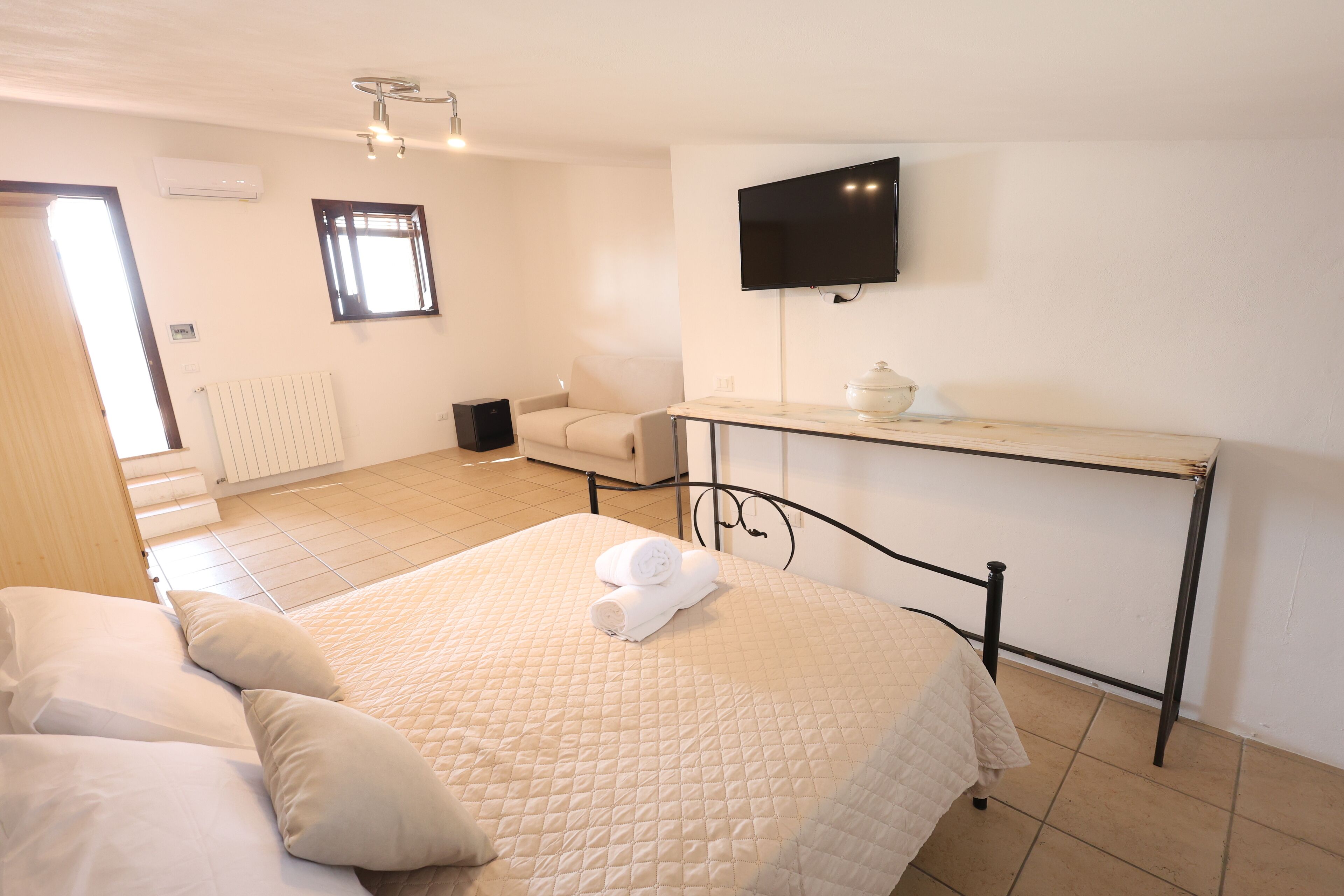 Een slaapkamer met een bed, nachtkastje, televisie en raam.