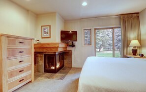Un dormitorio con chimenea, televisión, cama y ventana con cortinas.