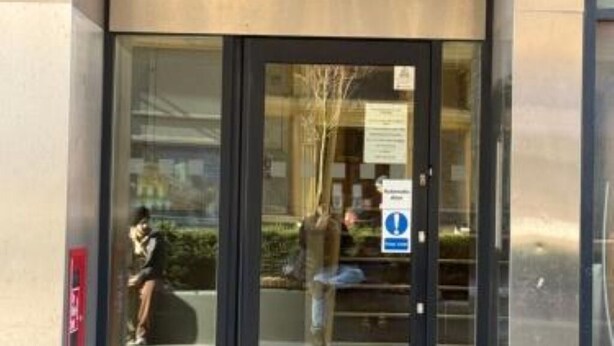 Entrada de un edificio con puerta de cristal y un cartel que indica una zona pública.
