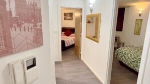 Un pasillo que conduce a un dormitorio con una cama, una mesita de noche y un calentador en la pared.