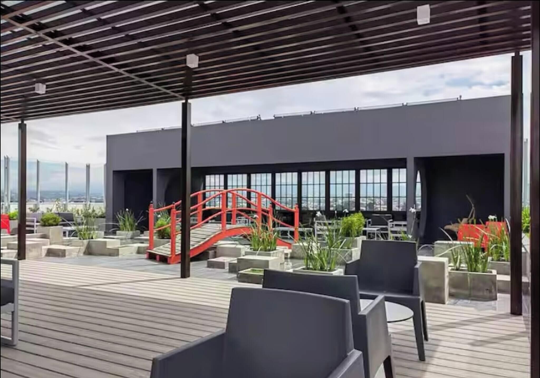 Una terraza en la azotea con mobiliario exterior, un puente rojo y vistas de la ciudad.